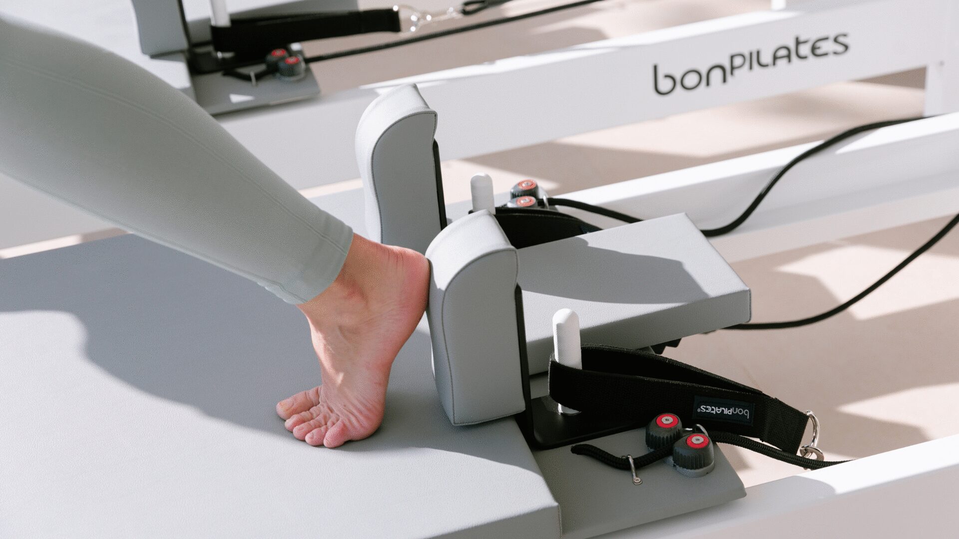 Ejercicio de piernas y pies en carro deslizante de máquina Reformer de Pilates.