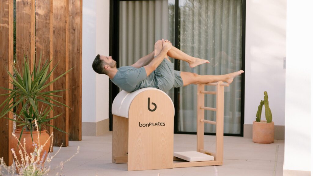 Un hombre realiza ejercicio de extensión de columna y control corporal en barril de Pilates o Spine Corrector.