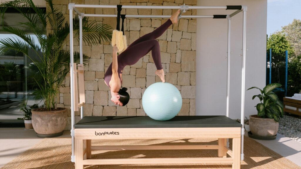 Ejercicio avanzado en suspensión boca abajo utilizando la estructura metálica del Cadillac de Pilates.